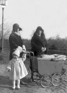 Two women wearing fashionable hats with a pram