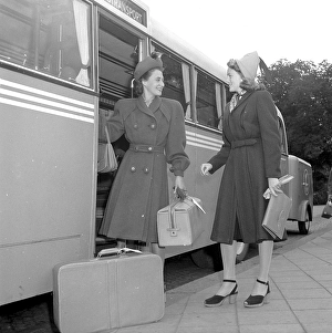 Women's fashion in the 1940s. A young woman in a typical 1940s coat, with matching hat, shoes, gloves and handbag. She steps off the bus carrying her luggage and is greeted by a lady friend also in a typical 1940s coat