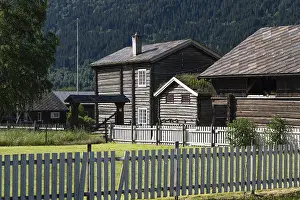 Wooden houses covered with slate tiles behind wooden fences in front of a wooded mountain landscape