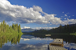Wooden jetty with lake, mountains and trees reflected in the water