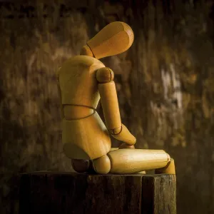 A wooden mannequin is positioned on a rough wooden surface