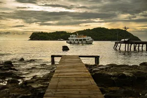 A wooden pier leads to a boat near an island