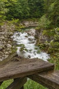 A wooden railing in the foreground with a view of a flowing mountain stream and rocks