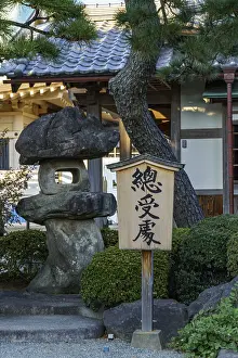 A wooden sign stands next to a large rock in a Japanese garden