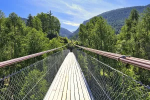 Wooden suspension bridge in a summer landscape with mountains and lush forest