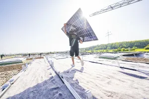 Worker carrying solar panel on an open roof in bright sunlight