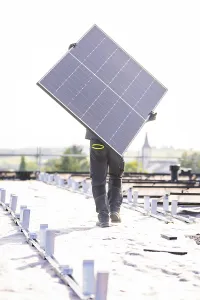 Worker carrying solar panel on a roof in bright light