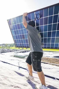 Worker carrying a solar panel on a roof under bright sunshine