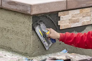 Worker installing wall tile cement with trowel and tile at construction site