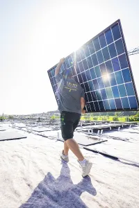 Worker moves solar panel on a sunny roof
