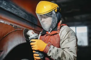 A worker in protective gear using a grinder on a vehicle
