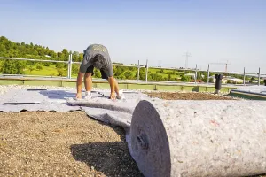 Worker on a roof rolling out a large underlay to prepare the ground
