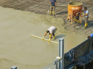 Workers smoothing concrete on a construction site while a concrete mixer stands in the background