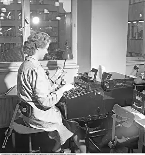 Workstation 1949. A woman sits at a kind of typewriter used to print banking documents like banking checks