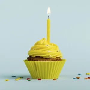 Yellow burning candles decorative muffins with colorful star sprinkles against blue backdrop