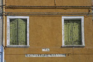 Yellow-orange house facade with 2 windows and weathered green wooden boards