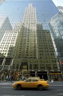 Yellow taxi driving in front of the glass facade of a skyscraper in Manhattan