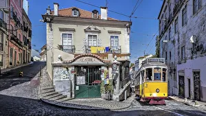 A yellow tram on a cobblestone street passing by a vintage building under a clear blue sky