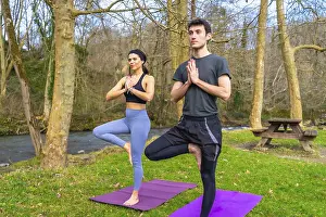 Yoga instructors performing the tree pose by a river in a forest