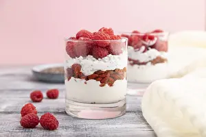Yogurt with raspberry, goji berries and chia seeds in glass on gray wooden background and linen textile