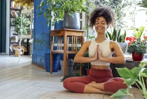 Young adult happy fit slim healthy African American ethnic woman wearing sportswear sitting in yoga pose at home in