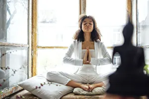Young adult happy fit slim healthy African American ethnic woman wearing white clothes sitting in yoga pose at home in