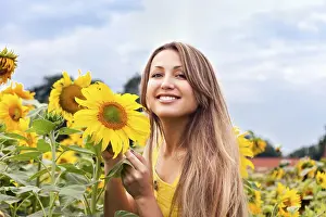 Young beautiful woman between sunflowers in a field