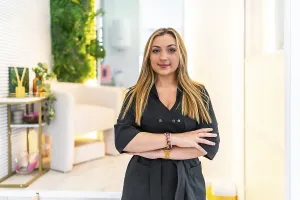 Young blond female beautician smiling with arms crossed in her beauty salon