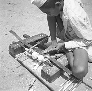 Young boy using portable rotating lathe applying lacquer wringtinforia wood, painting lacquer toys, Channapatna, Karnataka
