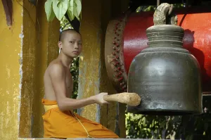 Young buddhist monk ringing the bell