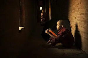 Young Buddhist novice monk reading book inside monastery