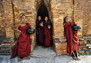 Young Buddhist novices holding alms bowls in front of the old monastery walls at the Shwezigon Pagoda in Bagan