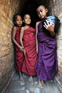Young Buddhist novices holding alms bowls in front of the old monastery walls at the Shwezigon Pagoda in Bagan
