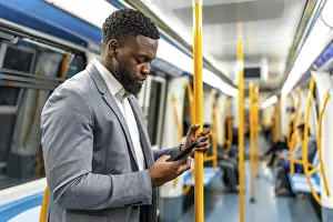 Young businessman using a smartphone while standing on a subway train during his daily commute through the bustling