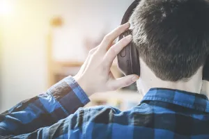 Young Caucasian man with checked blue shirt is listing to music with wireless headphones
