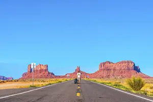 A young Caucasian man with white shirt and green backpack on the road to Monument Valley