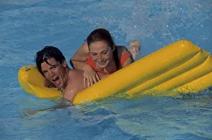 Young couple romps with yellow air mattress in swimming pool