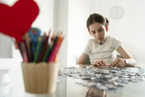 A young disabled girl with a tracheostomy focuses on assembling a puzzle at a table