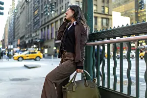 Young female executive communicating on her smartphone while leaning against a subway railing in midtown manhattan