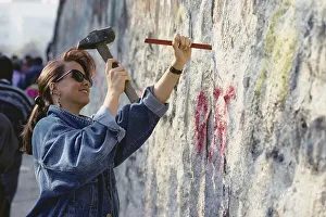 Young girl chisels splinters out from the Berlin Wall
