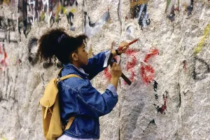 Young girl chisels splinters out from the Berlin Wall