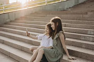 Two young girls sit together on sunlit stone stairs