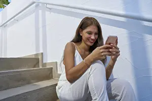 Young latin woman reading smarphone in a white stairway outdoor