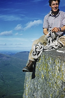 Young male climber sitting high up on a rock and holding a climbing rope, probably North Wales, Great Britain, around 1958