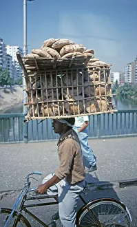 Young man on bicycle with bread basket on his head