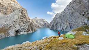 Young man with green tent at the turquoise mountain lake Kol Suu with rocky steep mountains