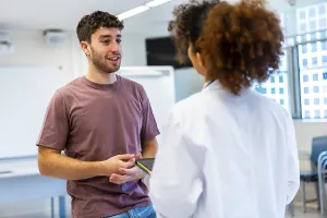 Young man holding a tablet, engaging in a conversation with a doctor inside a hospital room