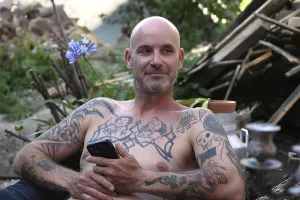 Young man with mobile phone, sitting in garden with bare upper body