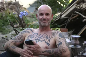 Young man with mobile phone, sitting in garden with bare upper body
