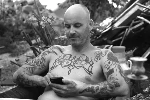 Young man on mobile phone, sitting in garden with bare upper body